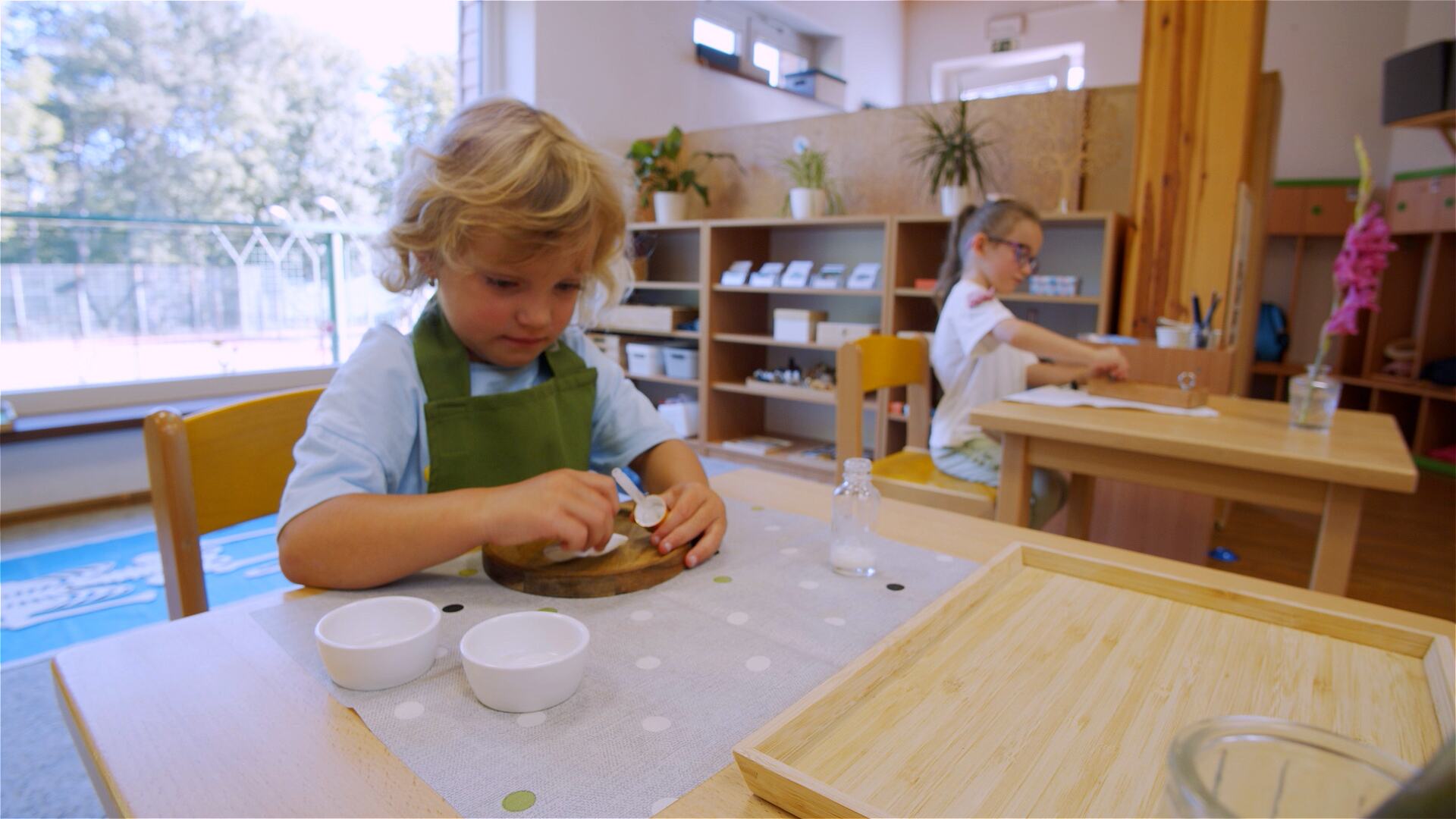A child in an apron working at a table in the classroom